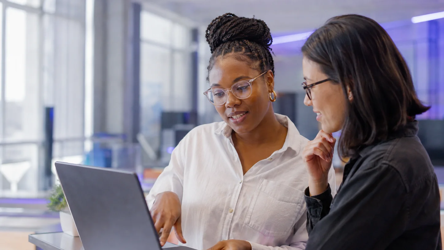 Two women collaborating on a laptop in a technology studio